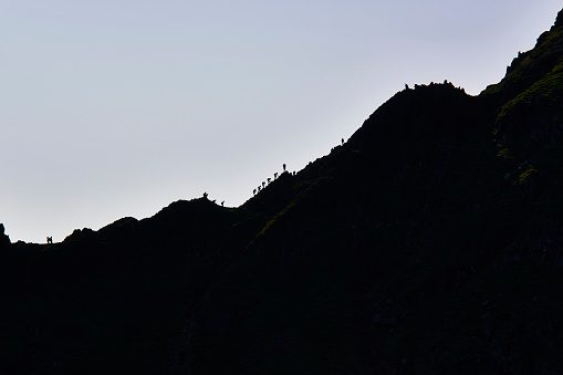 Silhouettes of group of hikers going uphill at sunset mountain