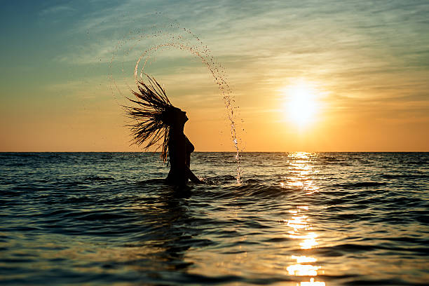 Silhouettes of woman jumping in ocean stock photo