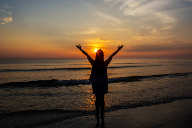 Silhouettes  of Woman raise hands up to the sunrise sky at the beach stock photo