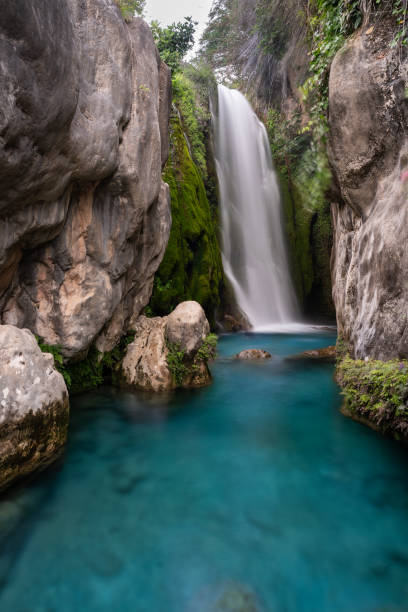 Silky waterfall wedged between rock walls with turquoise water stock photo