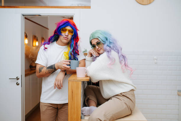 Silly looking couple in colorful wigs and sunglasses drinking tea in a kitchen stock photo