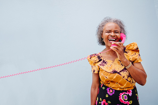 Senior  woman having fun with pink wintage telephone, isolated on blue wall background