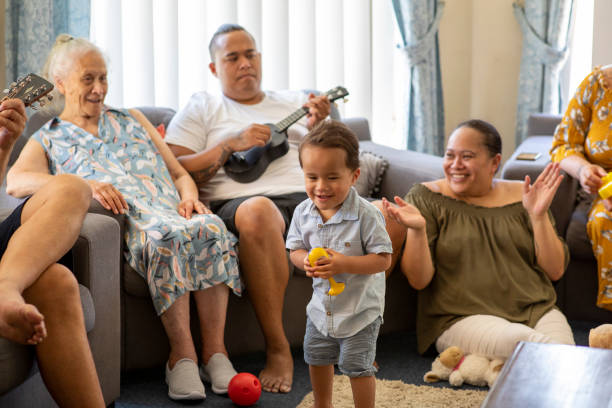 Singing Together Pacific Islander family sitting together at home. The young man is playing a ukulele and they are all clapping. pacific islander stock pictures, royalty-free photos & images