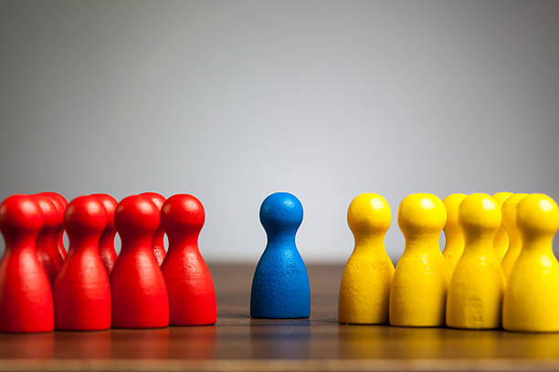 Single blue pawn figure between red and yellow groups stock photo