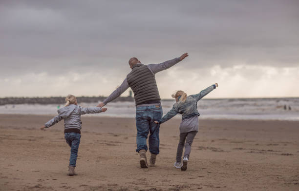 Single father and his daughters playing family games on a winter beach Handsome redhead single father and his blonde daughters playing family games on a winter beach divorce beach stock pictures, royalty-free photos & images