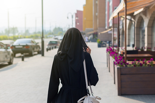 A single Muslim woman walks through empty big city rear view.