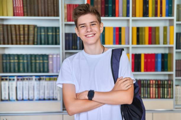 Single portrait of smiling confident male student teenager looking at camera in library stock photo