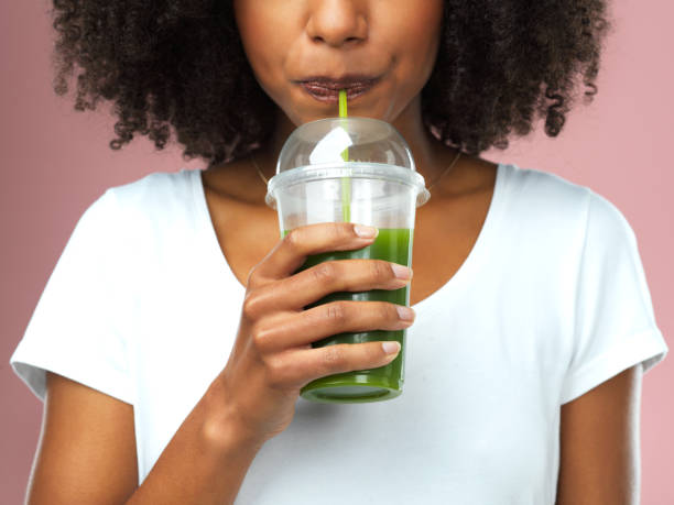 Sippin' on some green goodness Studio shot of an attractive young woman drinking green juice against a pink background drinking smoothie stock pictures, royalty-free photos & images