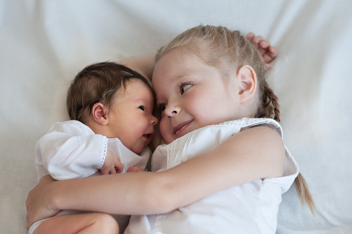 5 years old sister hugs her younger 2 weeks old brother