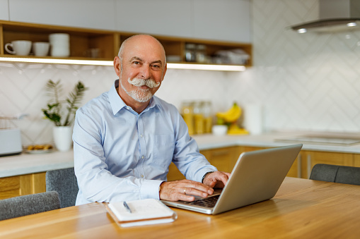 Mature man using laptop, kitchen in the background.