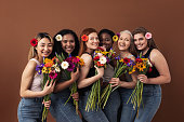 istock Six smiling women of different ages looking at camera in a studio. Happy diverse females with bouquets and flowers in their hairs standing together. 1330569546