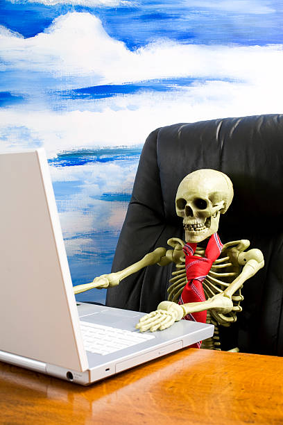 skeleton в завязками в креслом с ноутбуком на столе - human skeleton workin...