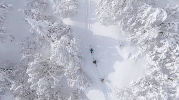 TOP DOWN: Ski tourers hike along an empty trail leading up a snowy mountain. stock photo