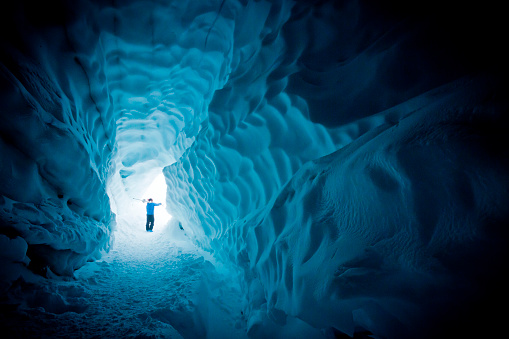 Male carrying skis on shoulders, walking out from glacier cave.