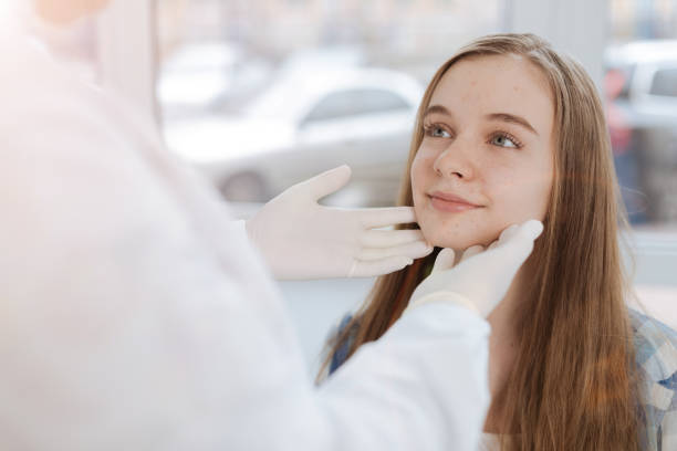 Skilled dermatologist examining patient skin in the clinic My first visit to the dermatologist. Delighted smiling cute girl sitting in the clinic and expressing positivity while doctor touching her face and examining problem dermatologist stock pictures, royalty-free photos & images