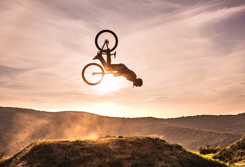 Mountain bike rider exercising at sunset and performing backflip against the sky. Copy space.