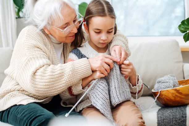 Skillful granny tutoring her granddaughter, teaching her how to knit stock photo
