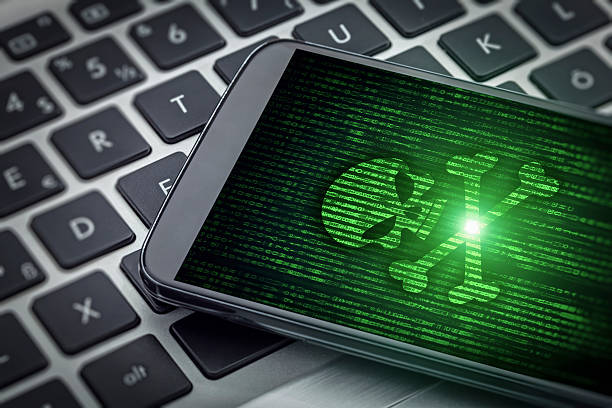 skull of death on smartphone screen Skull of death symbol on the screen of smartphone on laptop computer. There is data flowing background. Selective focus on screen of the phone. spyware stock pictures, royalty-free photos & images