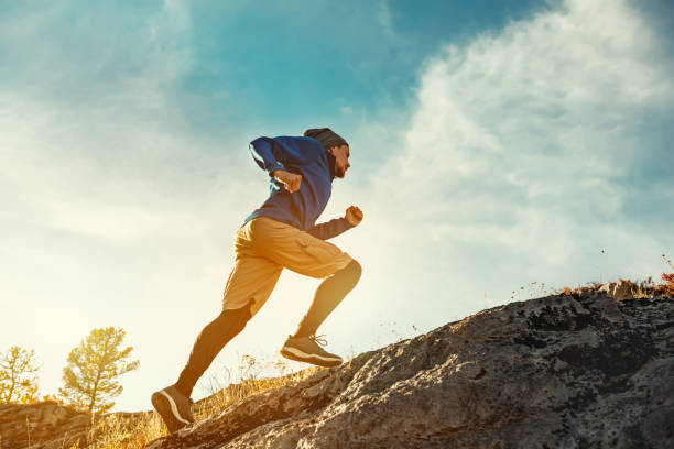 Skyrunner skyrunning crosscountry concept with young athlete on big rock Skyrunner athlete runs uphill against sunset or sunrise sky and sun. Skyrunning concept running stock pictures, royalty-free photos & images