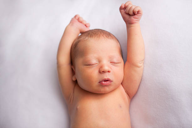 Sleeping Infant with arms raised, white blanket stock photo