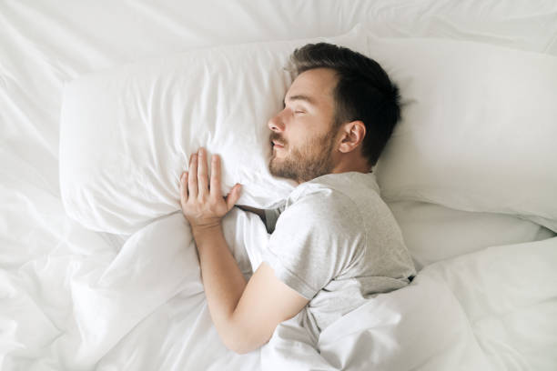 Sleeping man in white bed top view. Relaxed young bearded adult in cozy white bedroom having rest Lifestyle portrait of sleeping man sleeping stock pictures, royalty-free photos & images