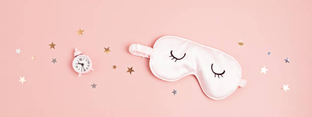 Sleeping mask and classic alarm clock on pink pastel background.  Minimal concept of rest, quality of sleep, good night, insomnia, relaxation. Flat lay, top view stock photo