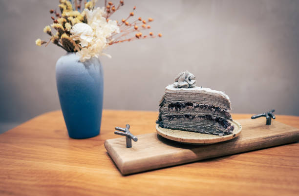 Slice of black cake on wooden table with blue vase on background. stock photo