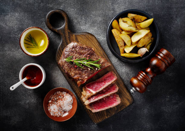Sliced grilled meat steak New York Striploin with sauce and potato on wooden board on grey background. stock photo