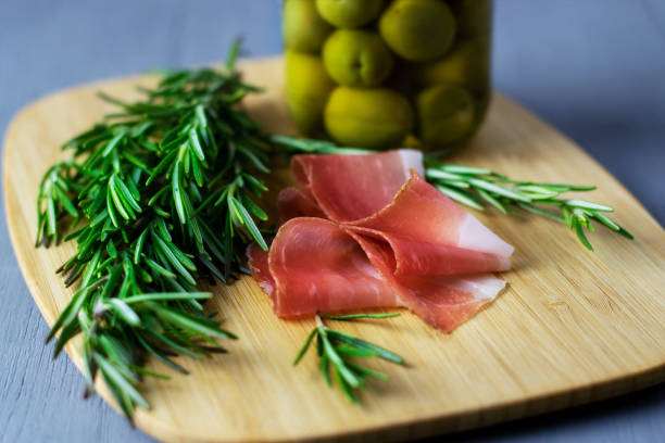 Sliced ham, Italian olives and rosemary on a wooden plate. stock photo