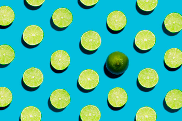 This is a fun brightly lit and colorful overhead photograph of sliced open geen limes lined in rows with a harsh shadow on a blue background.. There is one whole lime symbolizing individuality and being unique, different  or creative.