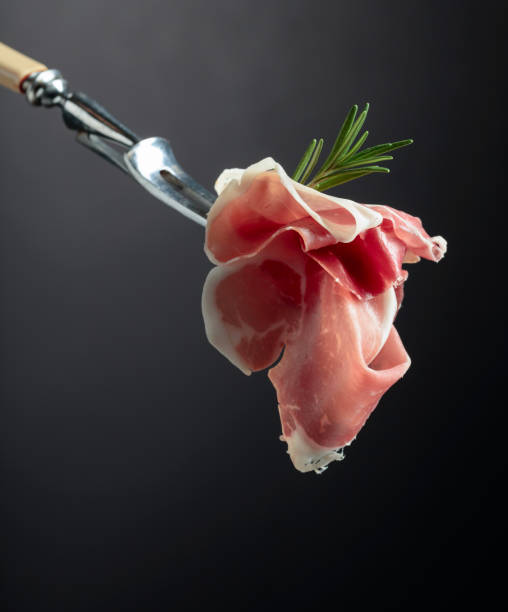 Sliced prosciutto with rosemary on a fork. Sliced prosciutto with rosemary on a fork, black background, copy space. prosciutto stock pictures, royalty-free photos & images