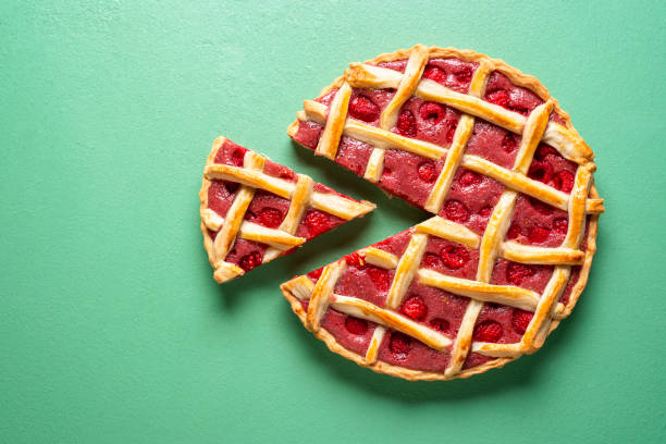 Sliced raspberry tart top view on a green background. Raspberries cake with lattice crust top view. Tasty home-baked pie with organic raspberries and white flour. Traditional lattice crust fruits filling pie above view. tart dessert stock pictures, royalty-free photos & images