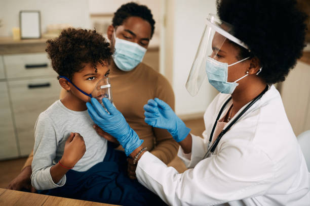 kleine zwarte jongen die astmabehandeling terwijl de arts hem thuis toe te schrijven aan covid-19 pandemie bekijkt. - astmatisch stockfoto's en -beelden