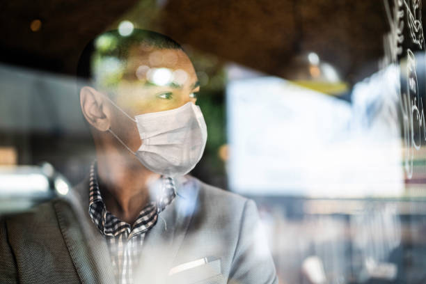 Småföretagare tittar ut genom fönstret med ansiktsmask