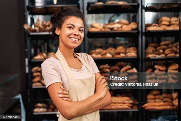 Small Business. Young woman in apron at bakery shop crossed arms posing to camera cheerful