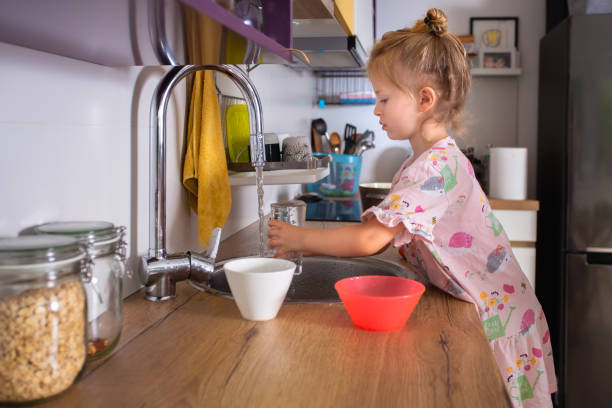 Small but already independent girl having a glass of water from the kitchen faucet stock photo