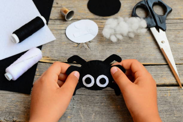 Small child holds a felt spider toy in his hand. Child made a Halloween felt spider crafts. Sewing workshop concept. Teaching a child to sew by hand stock photo