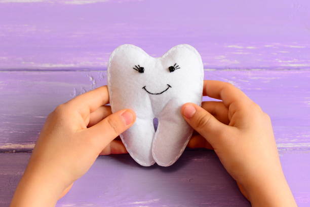 Small child made a felt tooth fairy. Small child holds a cute felt tooth fairy in his hands. Purple wooden background. Simple and fun kids crafts. Closeup stock photo