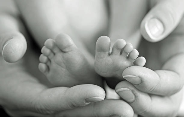Small feet Mother gently hold baby legs in hand. Black and white image with soft focus on babie's feet arrival photos stock pictures, royalty-free photos & images