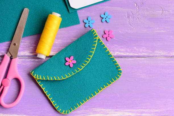 Small felt purse with flower wooden button. Scissors, thread, flower wooden button on a wooden background with copy space for text. Hand sewing for kids stock photo