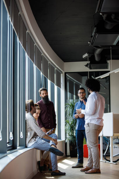 Small group of business people hanging out by the window, talking during coffee break stock photo