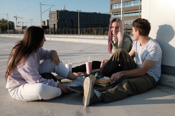 A small group of teenagers sitting outdoors and having fast food for a snack. Urban teenagers hanging out after school. stock photo