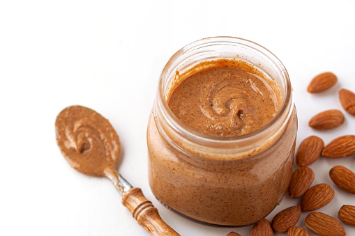 Organic almond butter with raw almonds in a glass jar on a white background with copy space