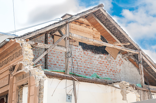 Small old and abandoned house roof demolished by the earthquake destruction closeup with blue sky above