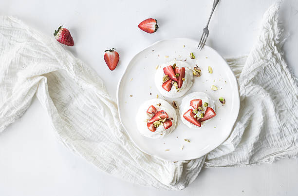 Small strawberry and pistachio pavlova meringue cakes with mascarpone cream Small strawberry and pistachio pavlova meringue cakes with mascarpone cream, fresh mint over white backdrop, top view pavlova dessert photos stock pictures, royalty-free photos & images