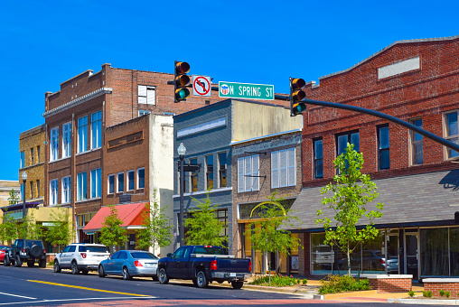 The main street downtown district with colorful retail storefronts and building facades in Tupelo, Mississippi. The image includes a deep blue sky, brown, orange and red colored buildings, a traffic signal and crosswalk.