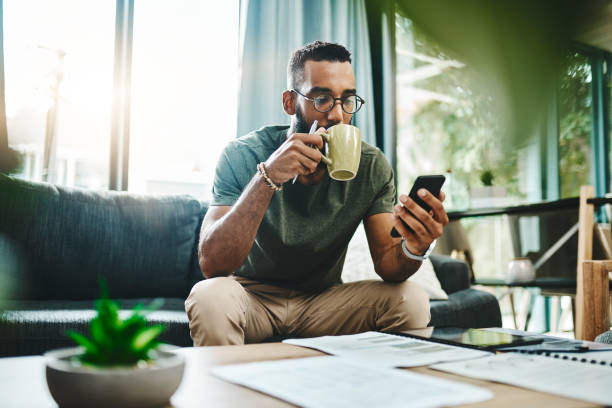 Smart apps make for smarter financial planning Shot of a young man using a smartphone while going over his finances at home coffee drink photos stock pictures, royalty-free photos & images