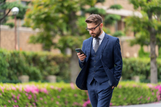 外出先でメッセージを読むスマートな服を着たビジネスマン - スーツ ストックフォトと画像