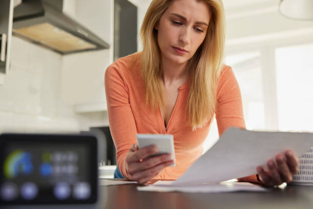 Smart Energy Meter In Kitchen Measuring Electricity And Gas Use With Woman Looking At Bills With Calculator stock photo