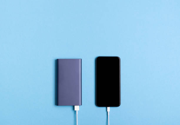 Smartphone charging with power bank on blue background stock photo